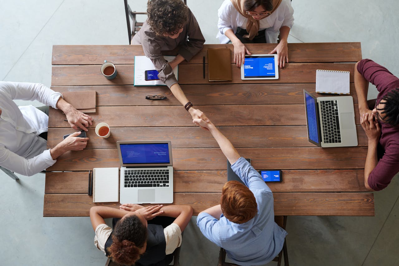 Servicios Overhead view of colleagues in a work meeting using laptops and tablets, emphasizing teamwork and technology.